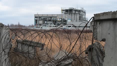 a destroyed factory on the outskirts of kramatorsk is seen through a broken fence and tangled barbed wire. a stark view of the industrial damage caused by the war in ukraine