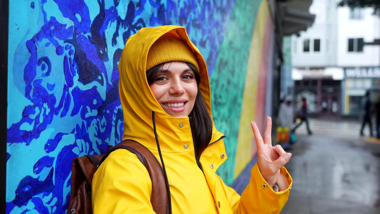 Giovane donna felice con impermeabile giallo che sorride accanto a un murale colorato
