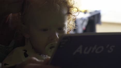 cute toddler girl reading a book with her grandmother, on the kitchen table