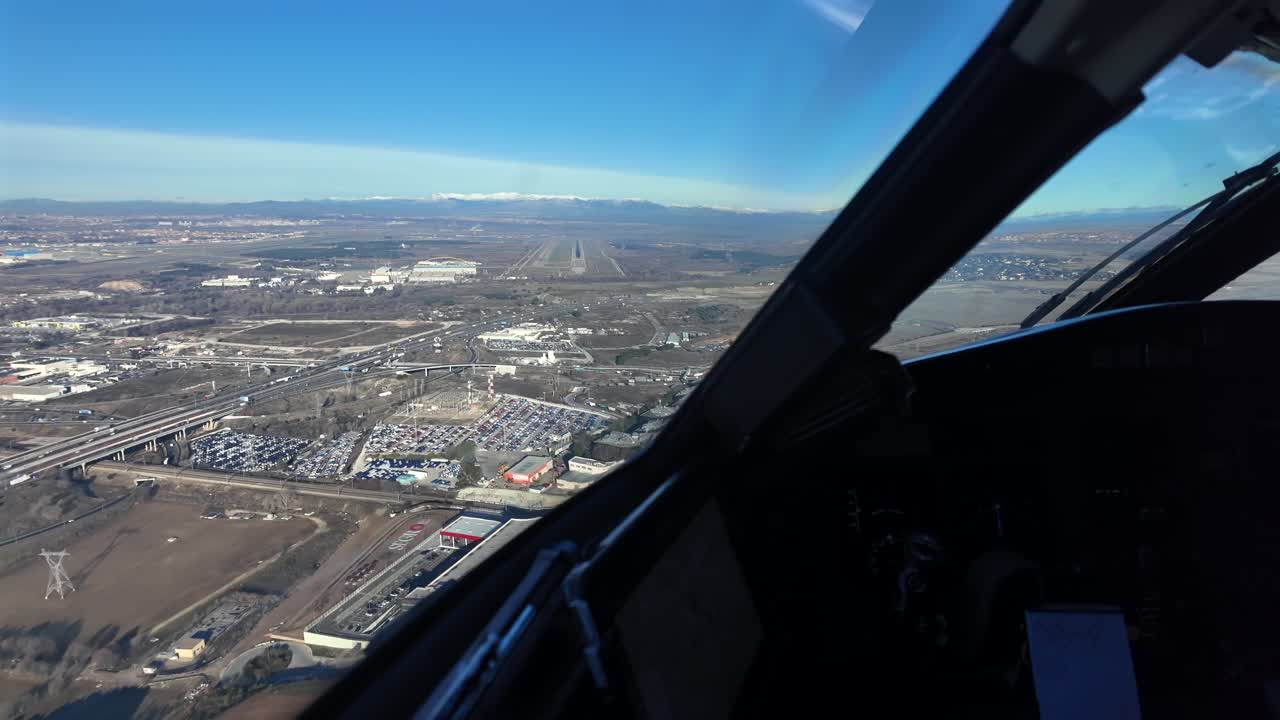 Pilot’s eye view in the final approach to Madrid airport, with a view of the runway ahear, and snow-capped mountains in the background under a bright winter sky