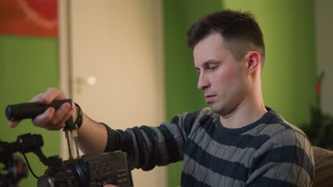 man adjusting camera with microphone in hands, focused on equipment setup in home studio. preparing for filming with clear attention to detail in creative workspace, soft natural lighting