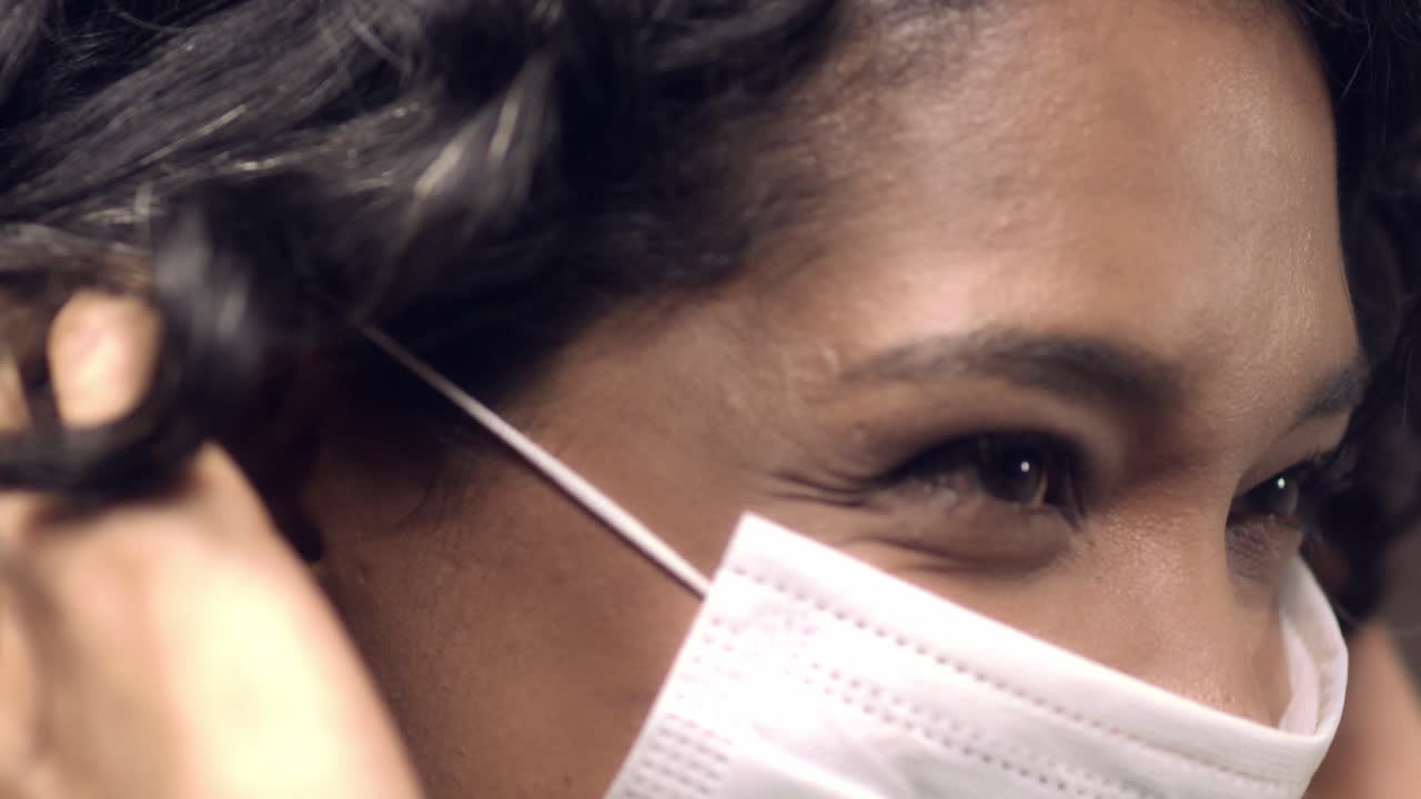 Young Latina, black or mixed race woman with a beautiful smile puts on a face mask for protection