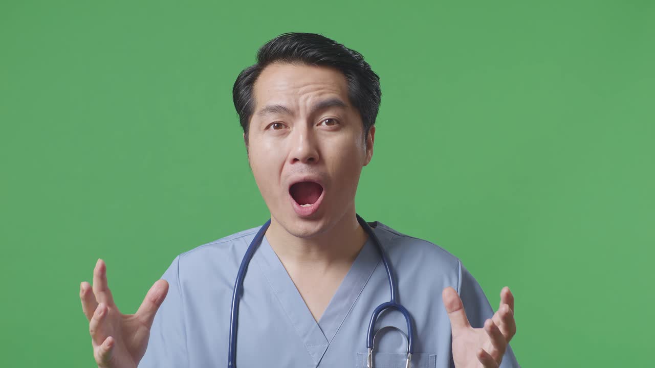 스테토스코프를 들고 있는 아시아 남성 의사의 가까운 모습, 몸짓, 손바닥, 와우라고 말하는 모습, 그리고 병원의 녹색 스크린 배경에서 웃는 모습