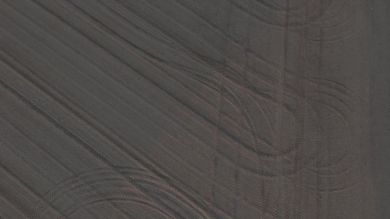 Freshly tilled seedbed in the Po Valley, Emilia-Romagna, Italy, shows fine harrowed soil and intersecting tractor tire tracks prepared for crop sowing, top down drone flyover.