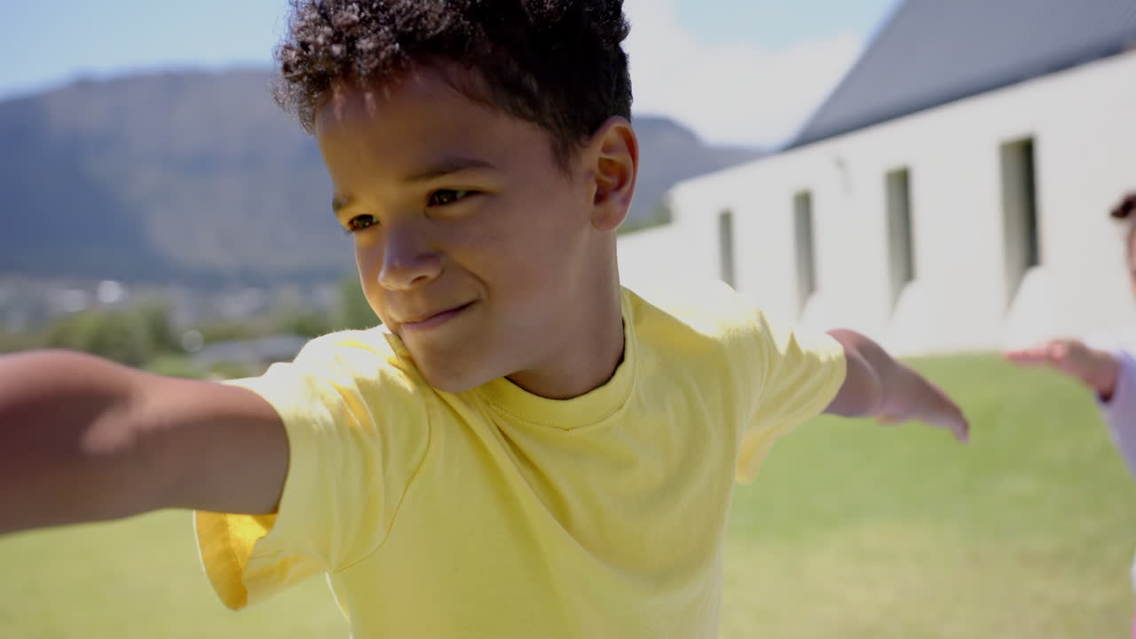 Biracial boy with curly hair is smiling outdoors in school, wearing a yellow shirt