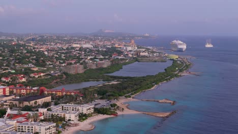 Willemstad-with-Cruiseship-and-sailing-ship-entering-port-during-sunset,-drone-ascend