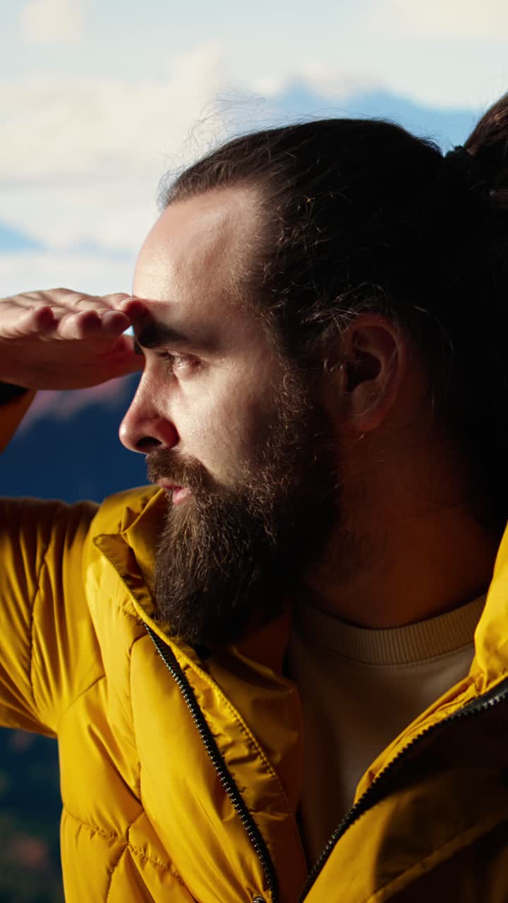 Hombre barbudo con chaqueta amarilla mirando la vista de la montaña