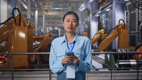 asian female with her smarphone with industrial robotic arms working, she observes by looking around before she come to concentrating with her smarphone