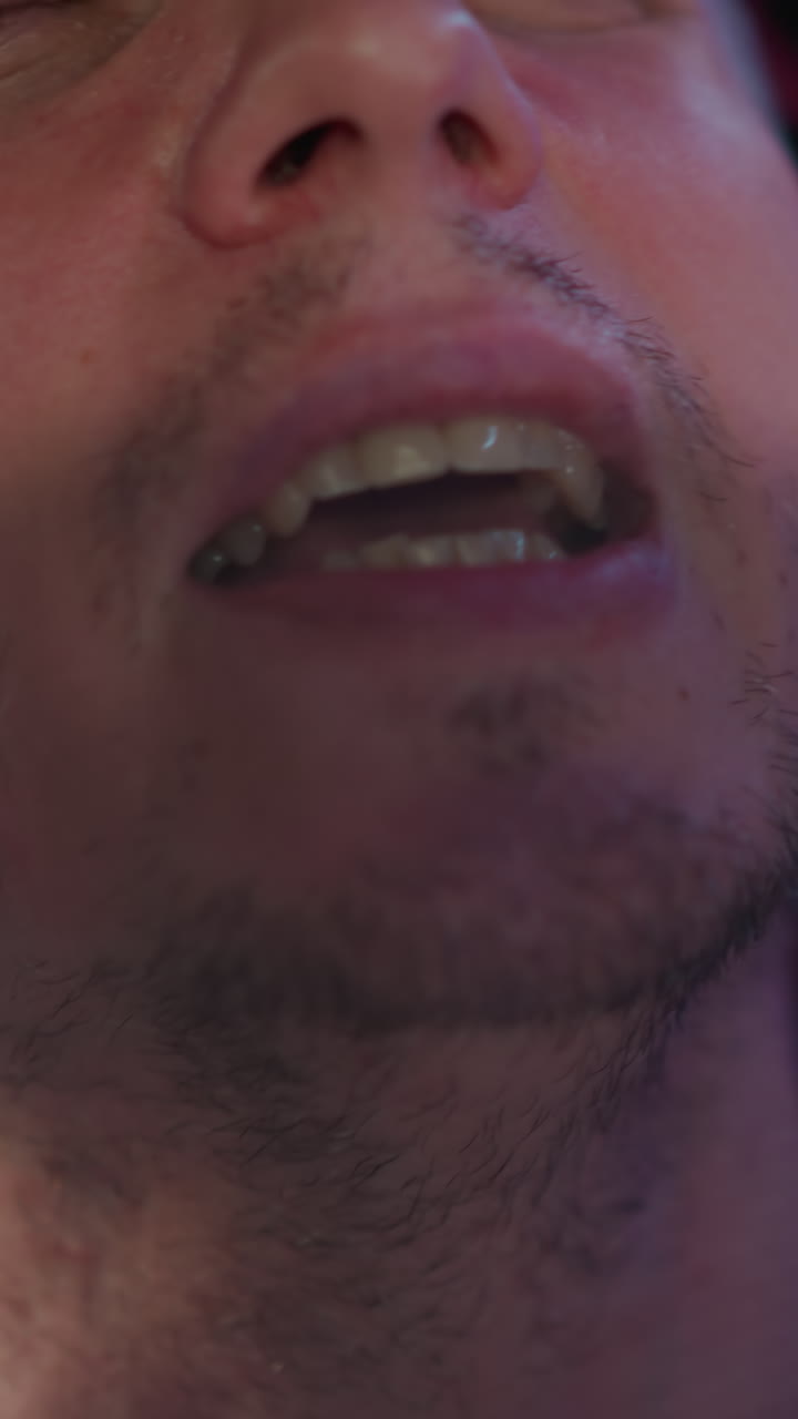 un primer plano de la cara de un hombre cantando apasionadamente con la boca abierta, con auriculares de estudio negros. la toma captura la intensidad de la actuación, en un fondo rojo