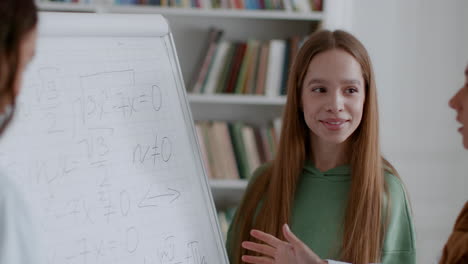young woman explaining mathematics on a whiteboard in a classroom