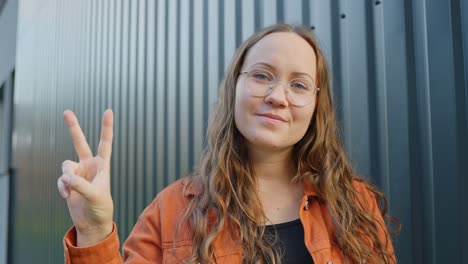 Mujer-Rubia-Con-Gafas-Mostrando-El-Signo-De-La-Paz,-Irradiando-Victoria-Con-Una-Sonrisa