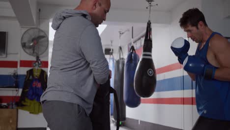 caucasian man training with coach in boxing gym