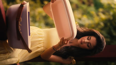 hermosa mujer joven abriendo la caja fría de diseño de moda, vestido de verano amarillo, sorpresa misteriosa, luz del sol de mal humor, jardín verde exuberante, cerrado vertical cinematográfico en cámara lenta