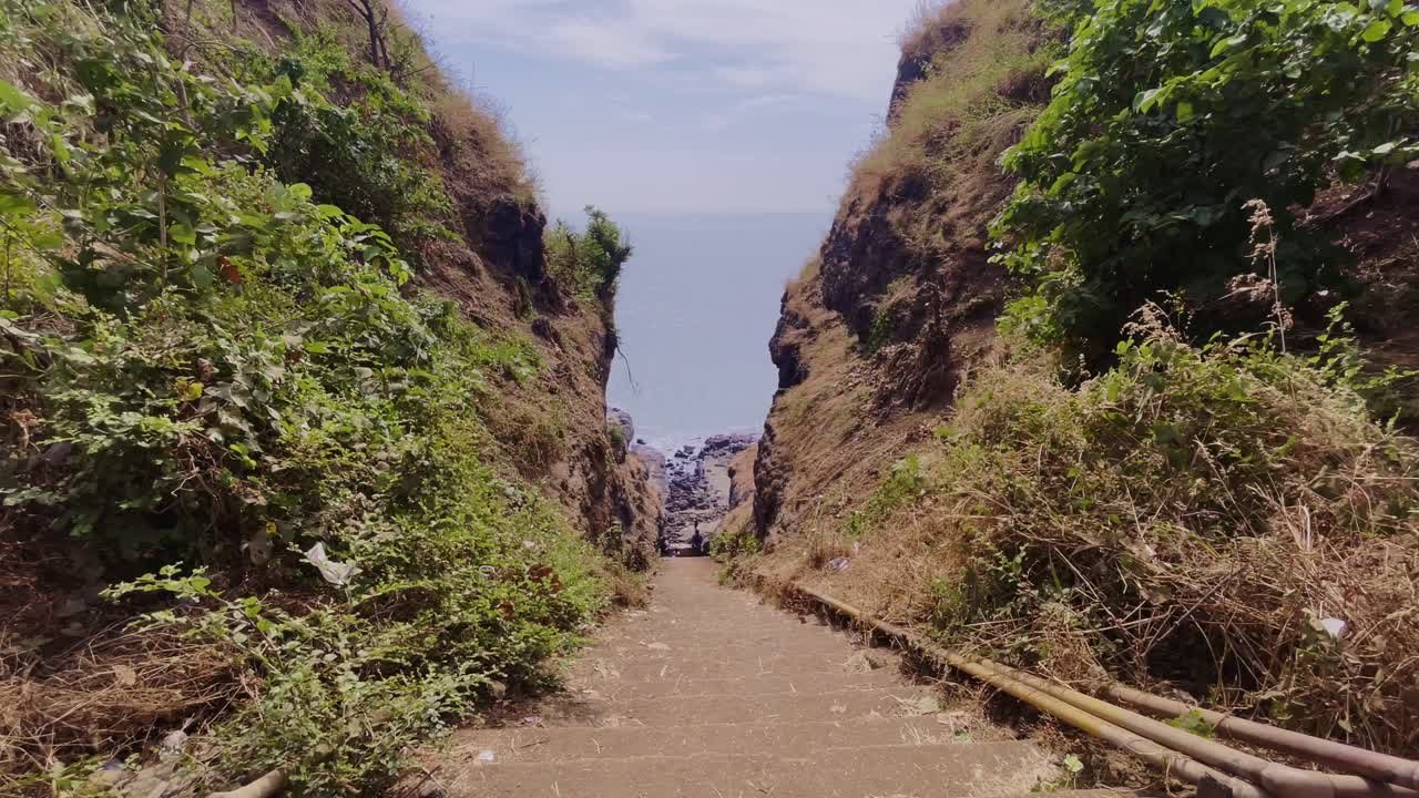 A serene road winds between two lush green hills under a bright sunny sky in Harihareshwar, Maharashtra, offering a peaceful drive through beauty 4K