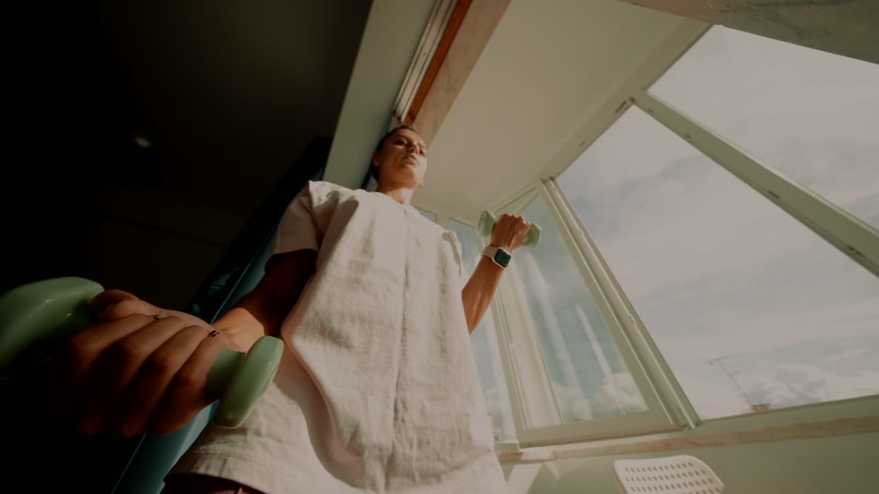 Woman working out with dumbbells by the window