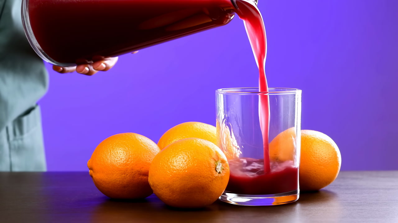 Fresh Oranges Red Juice Pouring Into Glass, Hands In Green Apron Tilt Pitcher Over Clear Glass On Wooden