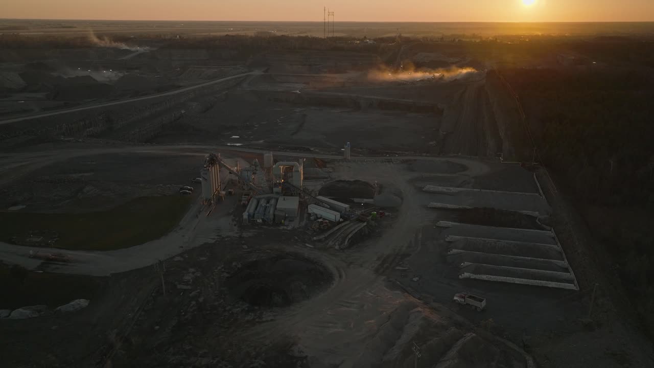 Reversing cinematic drone shot of a stone quarry at dusk with stockpiles and concrete equipment in foreground