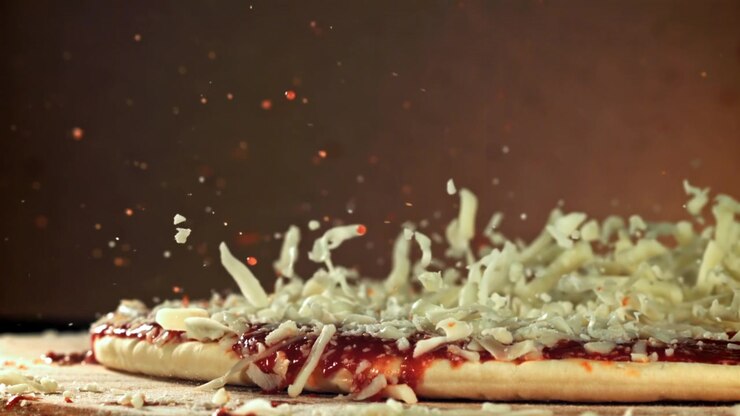 Rallentatore di formaggio grattugiato che cade su pizza cruda