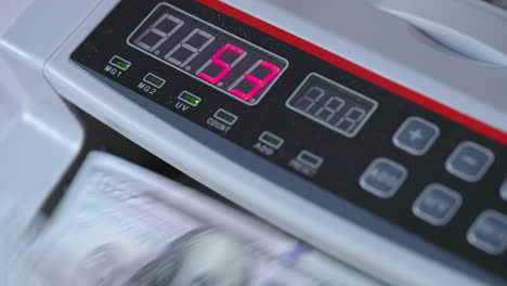 electronic scoreboard of cash counting machine with numbers on. dollar bills rotating in the device. close up.