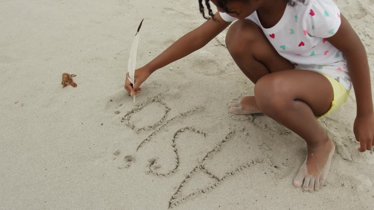Girl writing Social in sand with feather on beach drawing social media icons rising swirling fading
