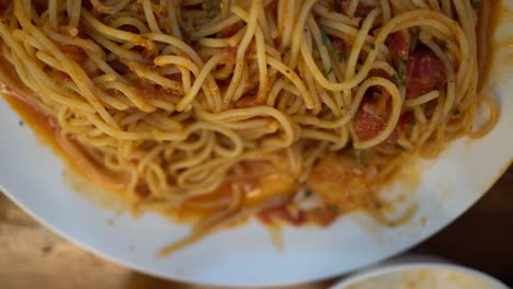 a little girl eats tomato seafood spaghetti in a restaurant. over look.