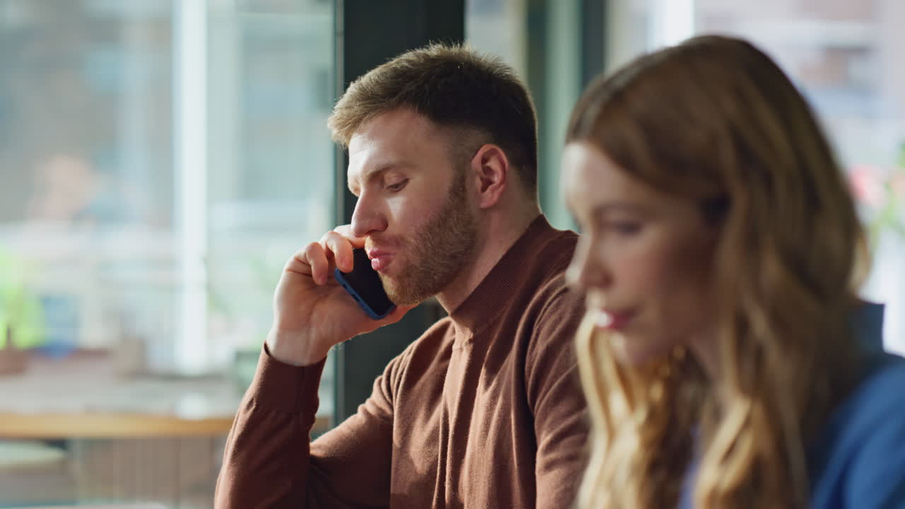 Professional man talking smartphone in office desk with woman coworker closeup
