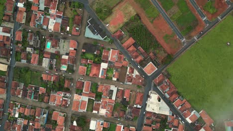 arial view going down rotating - a neighborhood with red roof houses surrounded by green hills during a cold foggy day - bueno brandao, minas gerais, brazil