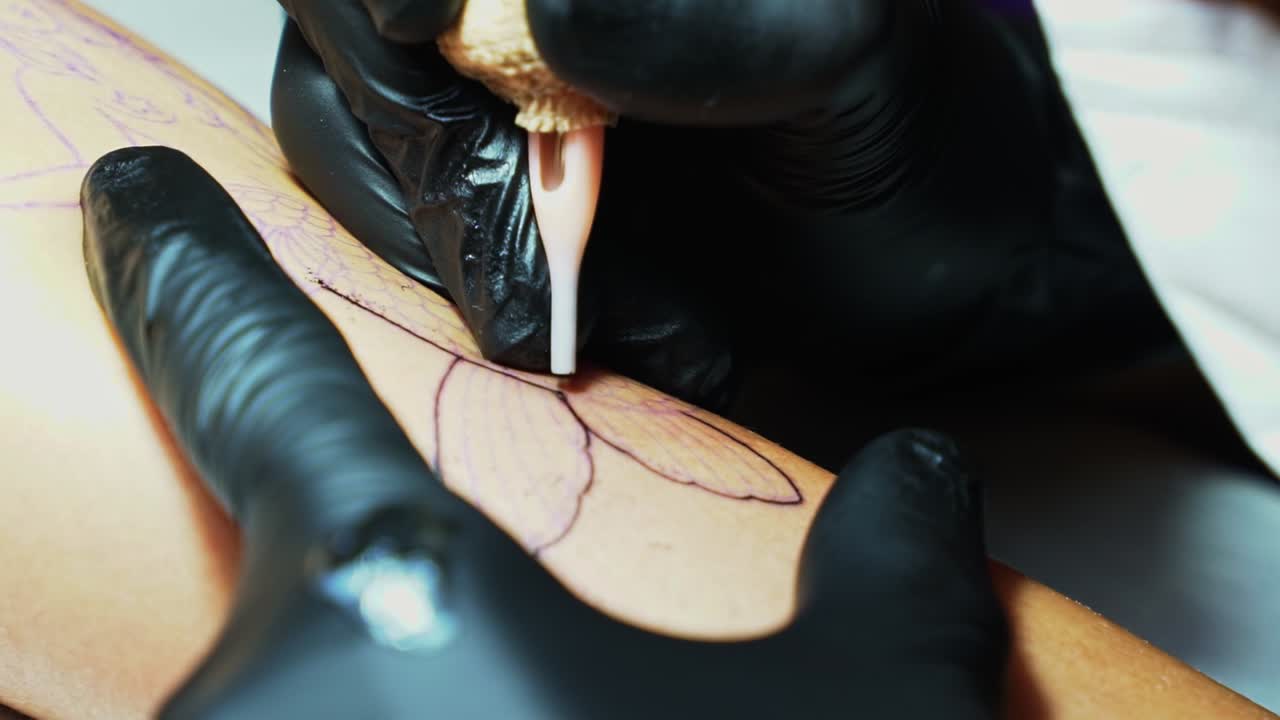 Primo piano, ripresa a mano libera al rallentatore dell'ago di un tatuatore che penetra la pelle mentre segue il contorno temporaneo dell'immagine desiderata in una stanza buia dello studio.