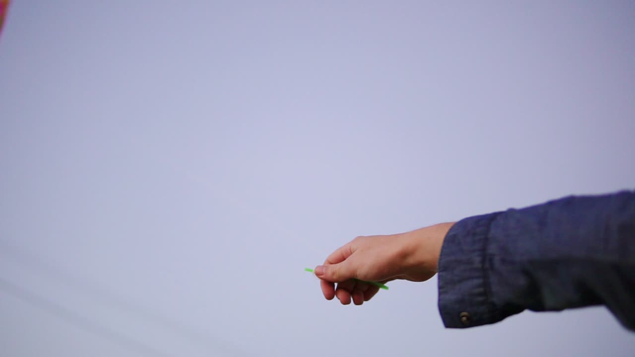 Close Up view of woman's hand holding colorful kite in the evening. Colorful kite in the sky on the background. Slow Motion shot