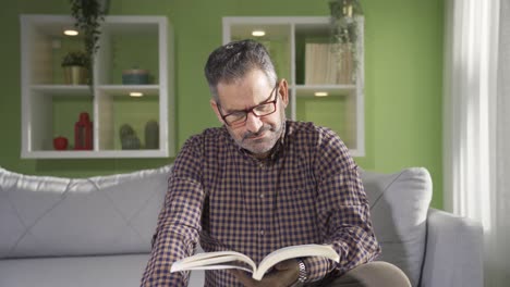 un hombre maduro y feliz relajándose en el sofá mientras lee un libro en casa. jubilación, vida en casa, concepto de estilo de vida.