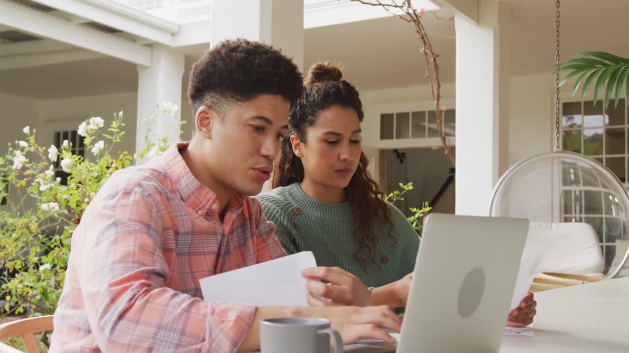 video de una pareja biracial usando una computadora portátil en el jardín