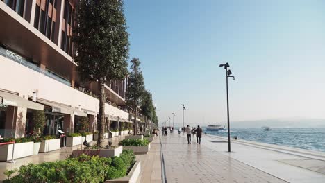 people walking along a waterfront promenade with buildings in the background