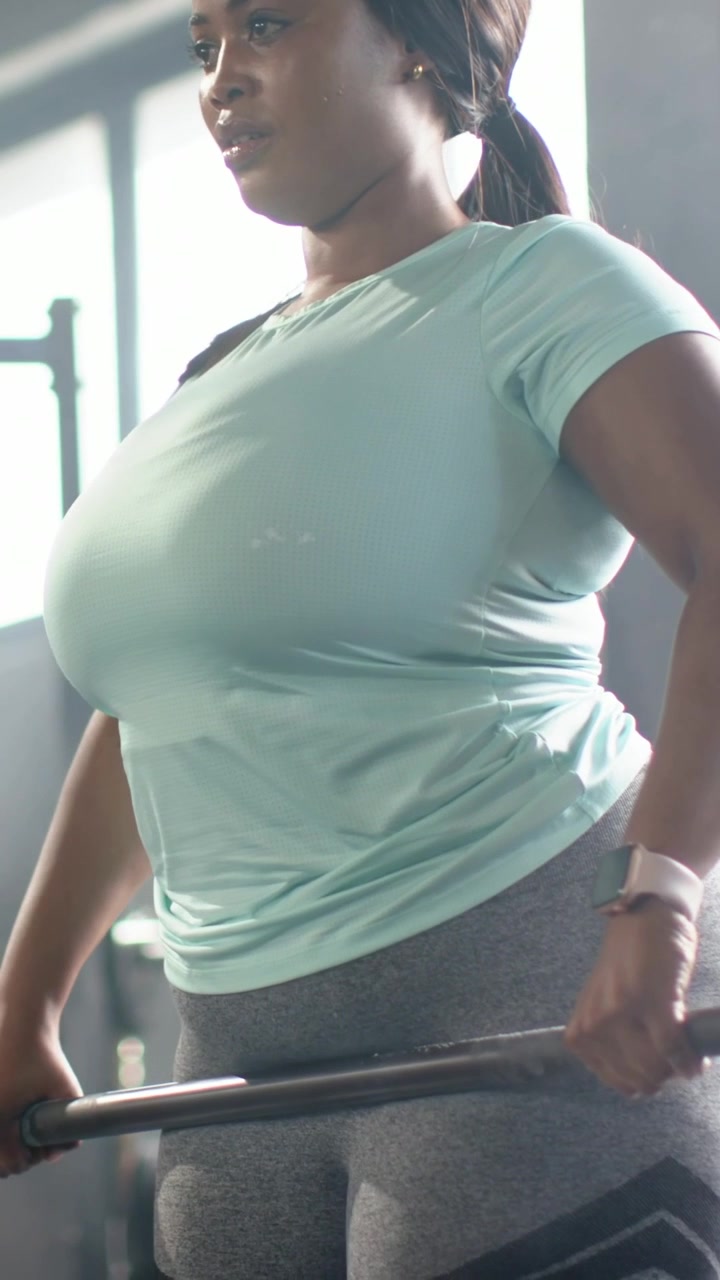 Video verticale: Donna adulta con un top color verde acqua, si china per afferrare una sbarra e solleva pesi in palestra per allenare la forza.