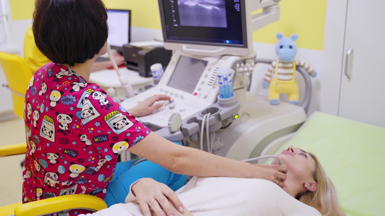 Ultrasound scanning of thyroid gland. Doctor looks at the screen of a computer during ultrasonic diagnostic. Female patient visiting doctor.