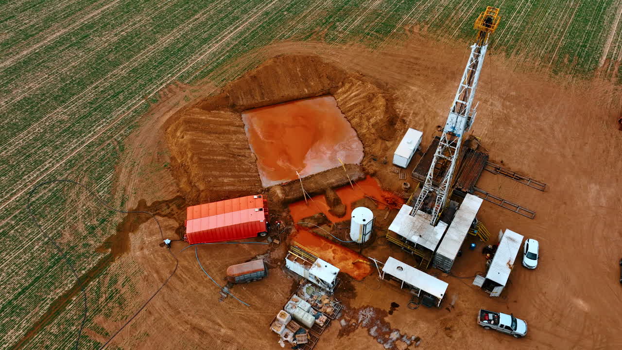 Oil production site with one derrick in the middle. Drone footage approaching the square pool with orange water.