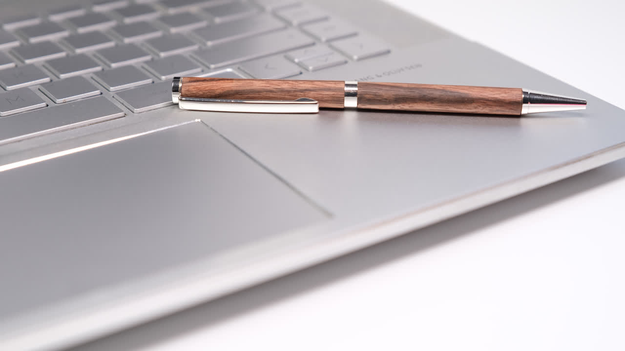 Close up shot of a pen resting on a laptop placed on a white table creating a simple and minimal writing concept