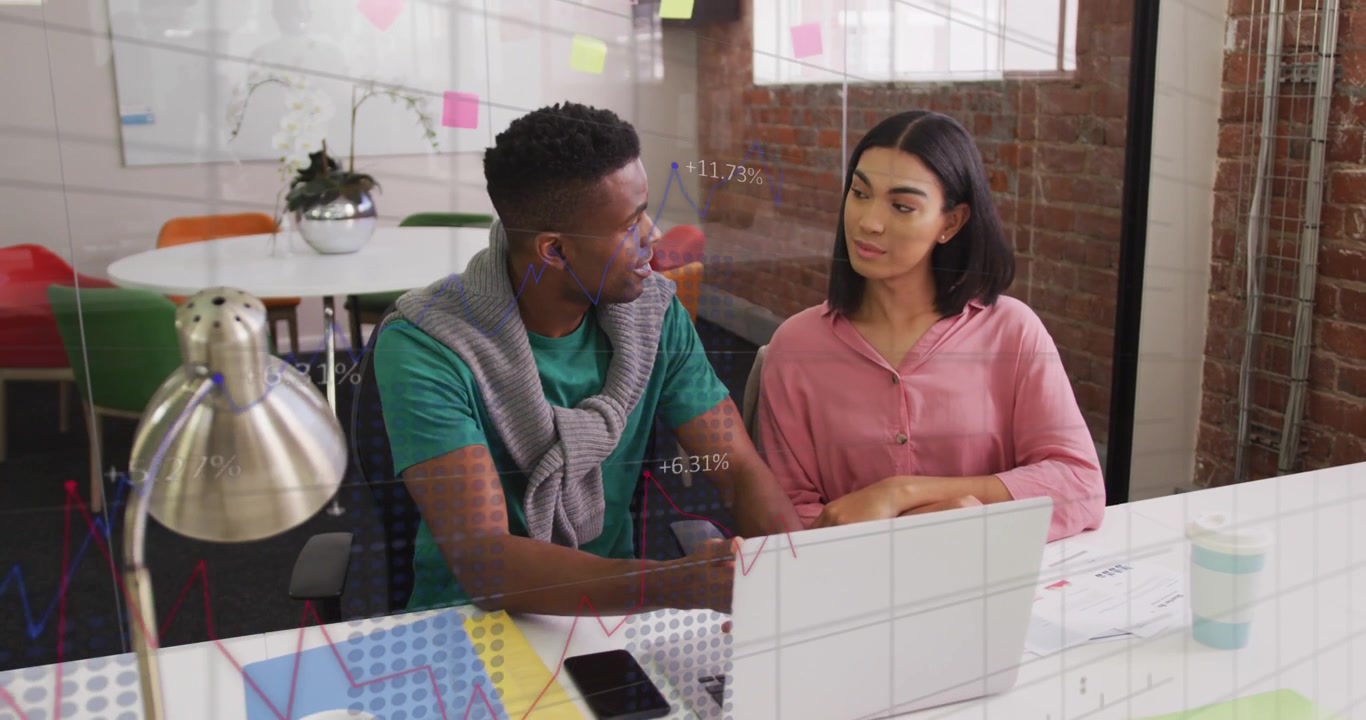 Man opening laptop and speaking while woman nodding, office charts animating from laptop for review