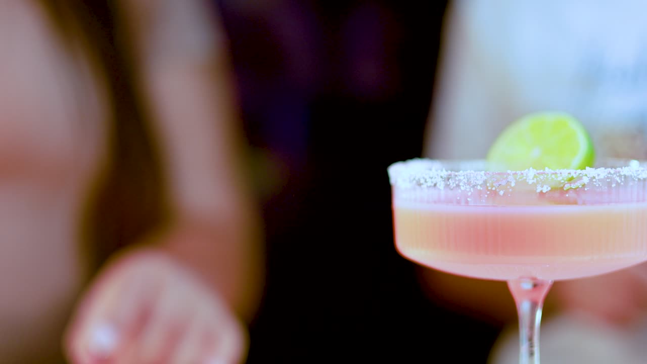 Uma série de coquetéis coloridos segurados por pessoas em um ambiente social animado e com iluminação suave, destacando bebidas vibrantes e uma atmosfera festiva