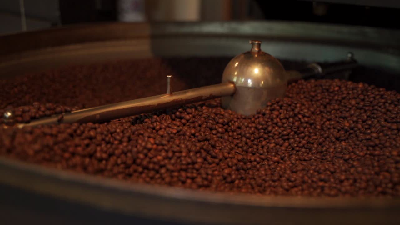 Traditional golden open coffee roasting machine roasting fresh coffee beens turning them around with its shovel, beans falling slowly in slowmotion roaster