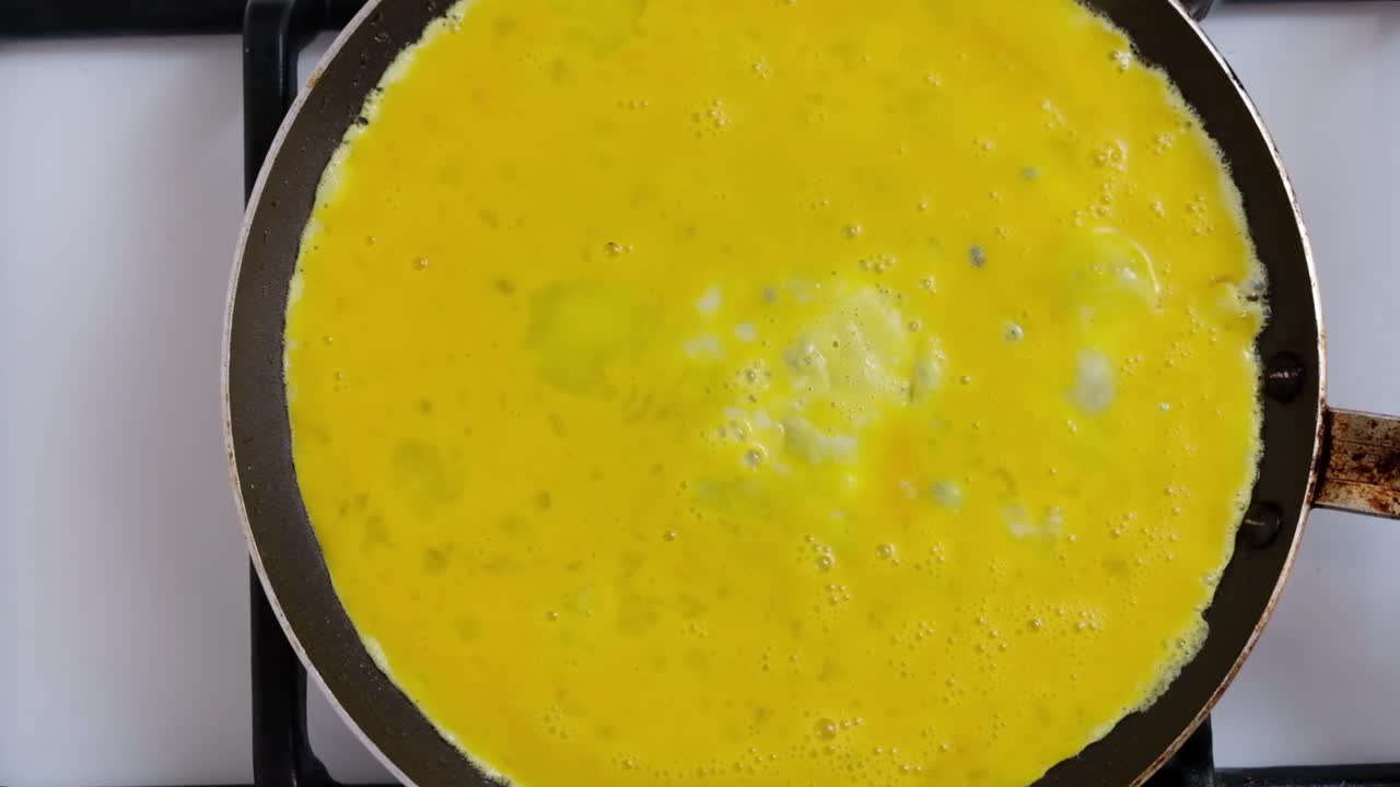 Woman pouring beaten eggs on a pan to make an omelette