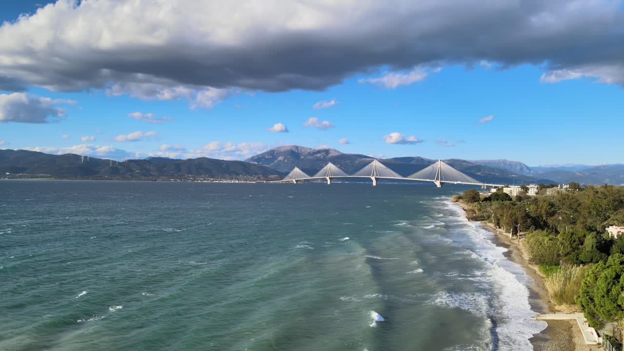 風の強い日、ギリシャのパトラス近郊の海岸に打ち寄せる波。遠方にはリオ・アンティリオ橋が見える。