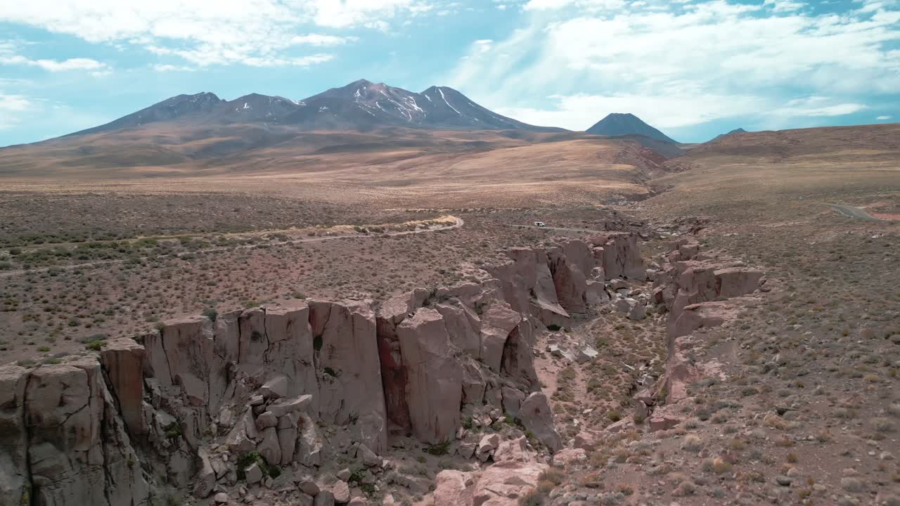 drone volando sobre el borde de un gran cañón en el desierto chileno con un volcán en el fondo