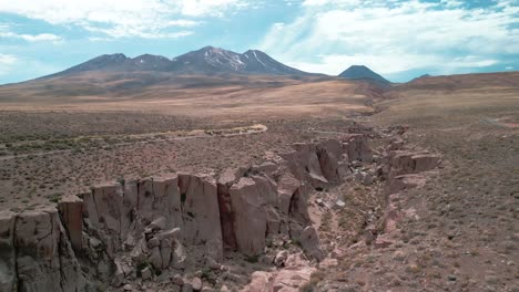 Drone-flying-over-the-edge-of-a-big-canyon-in-the-Chilean-desert-with-a-volcano-on-the-background