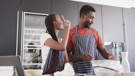 Feliz-Pareja-Afroamericana-En-Delantales-Horneando-Juntos-Usando-Tableta-En-La-Cocina,-Cámara-Lenta