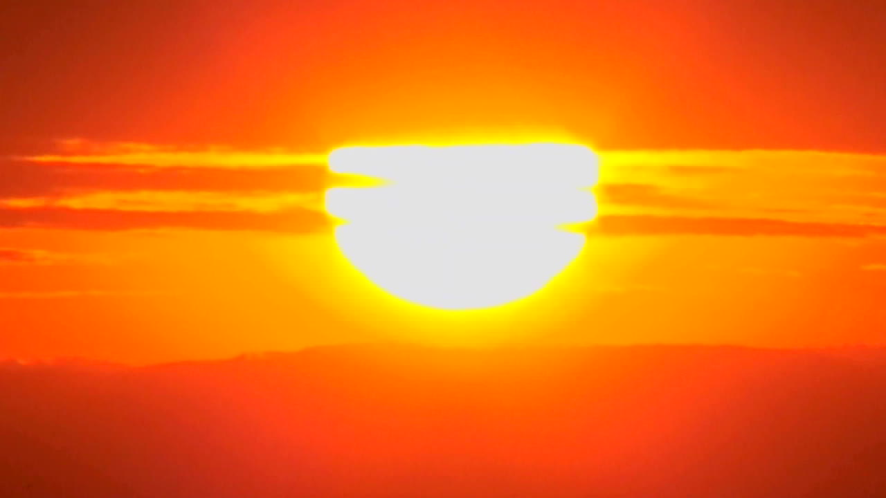 el sol se pone lentamente a través de las nubes en una enorme bola naranja