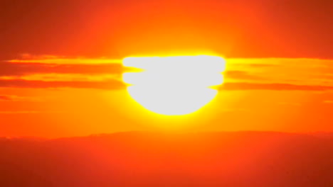 el sol se pone lentamente a través de las nubes en una enorme bola naranja