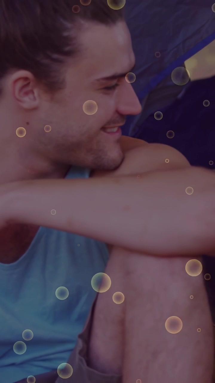 Vertical video: Man sitting in tent, camera panning, turning to friend, bubbles floating over man