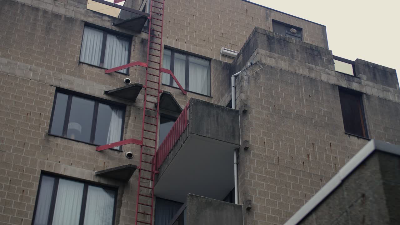 Close-up of an aged concrete residential building featuring a red metal ladder, balconies, and large windows