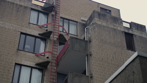 close-up of an aged concrete residential building featuring a red metal ladder, balconies, and large windows