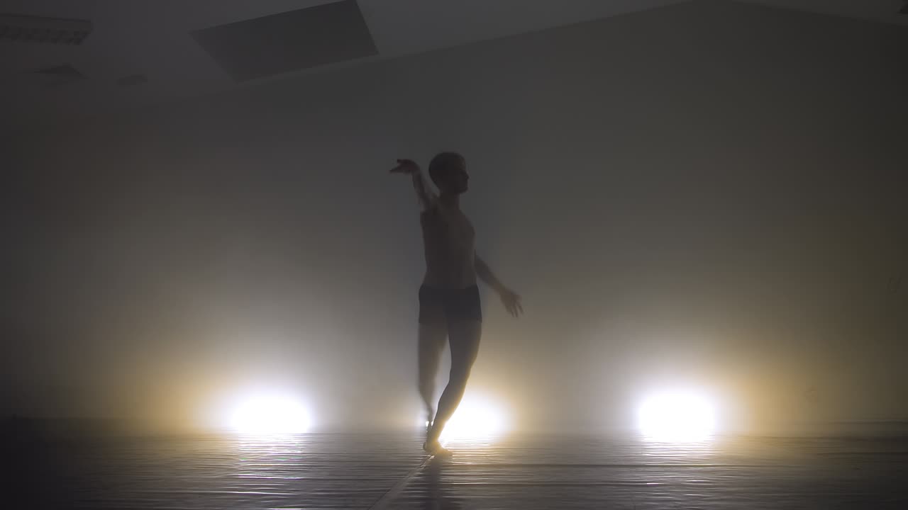 Slow shutter effect of moving modern male dancer in dark studio with backlights and dense smoke